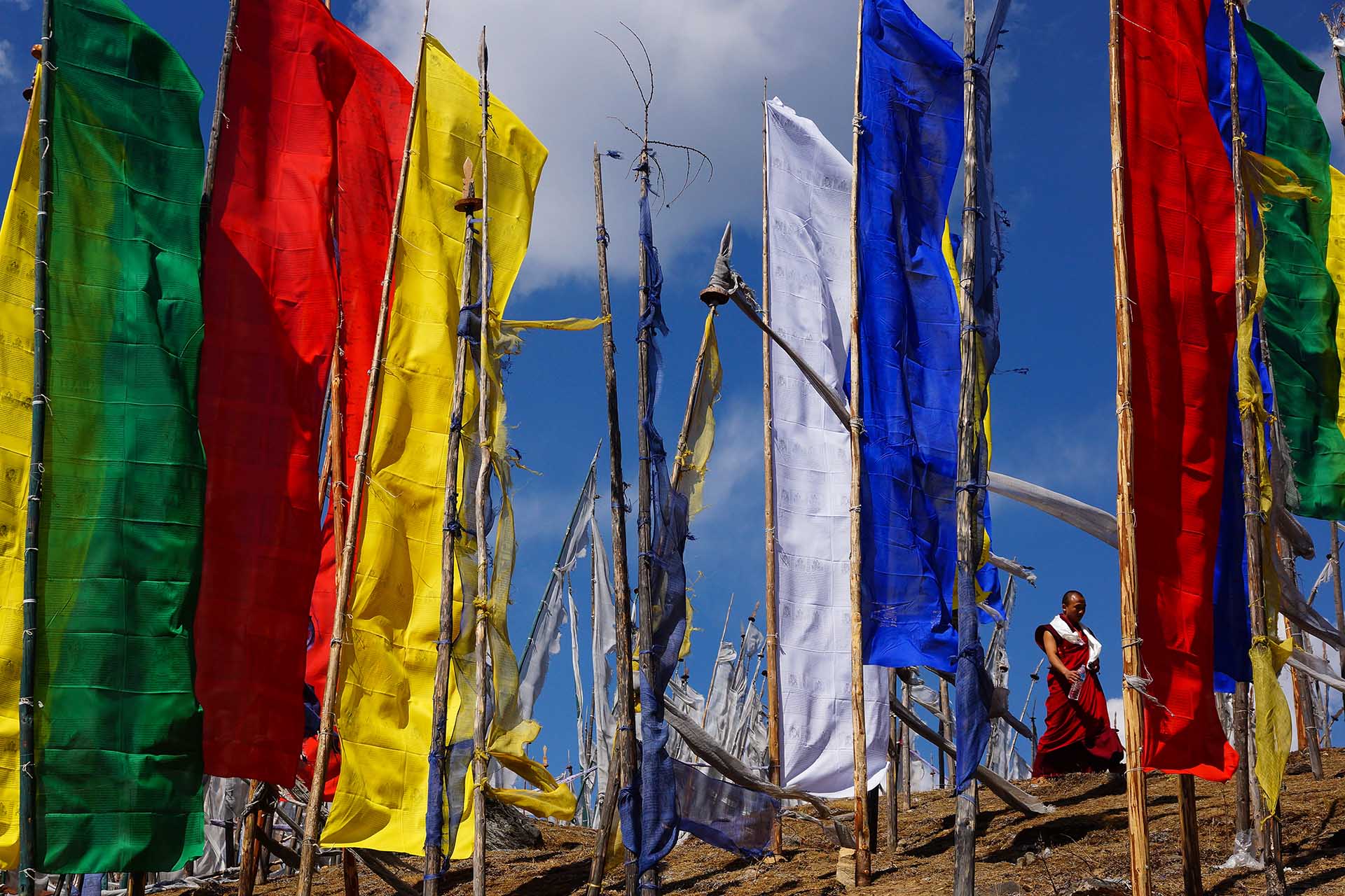 in rood gewaad geklede monnik loopt tussen grote staande gebedsvlaggen in Bhutan