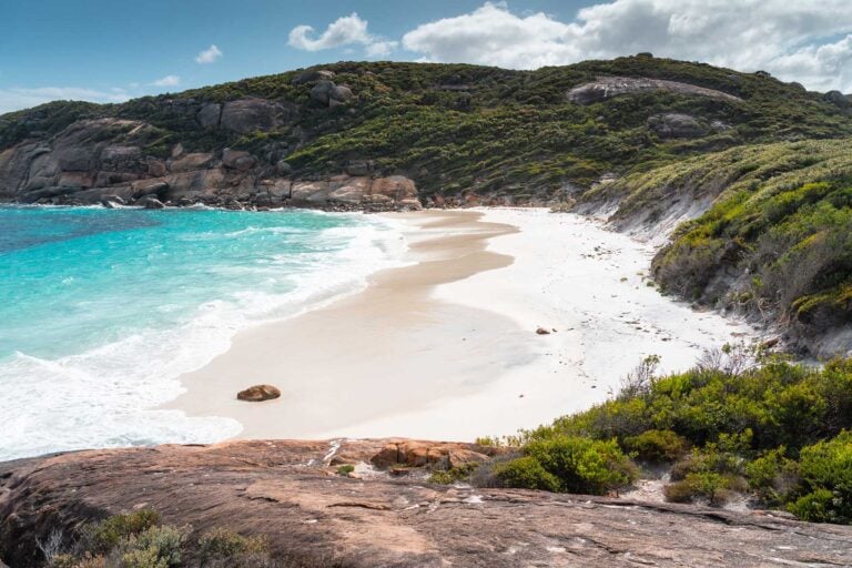 Baai met wit strand, gladde rotsen en groene struiken