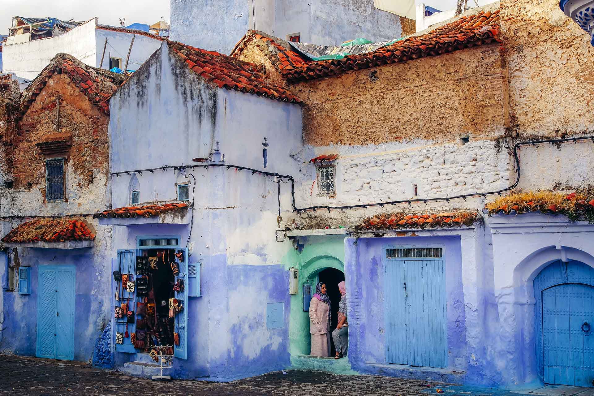 twee Marokkaanse vrouwen praten in de deuropening van een huis in het blauwgeschilderde Chefchaouen