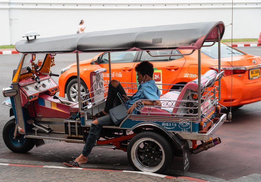 chauffeur kijkt achter in tuk tuk op telefoon